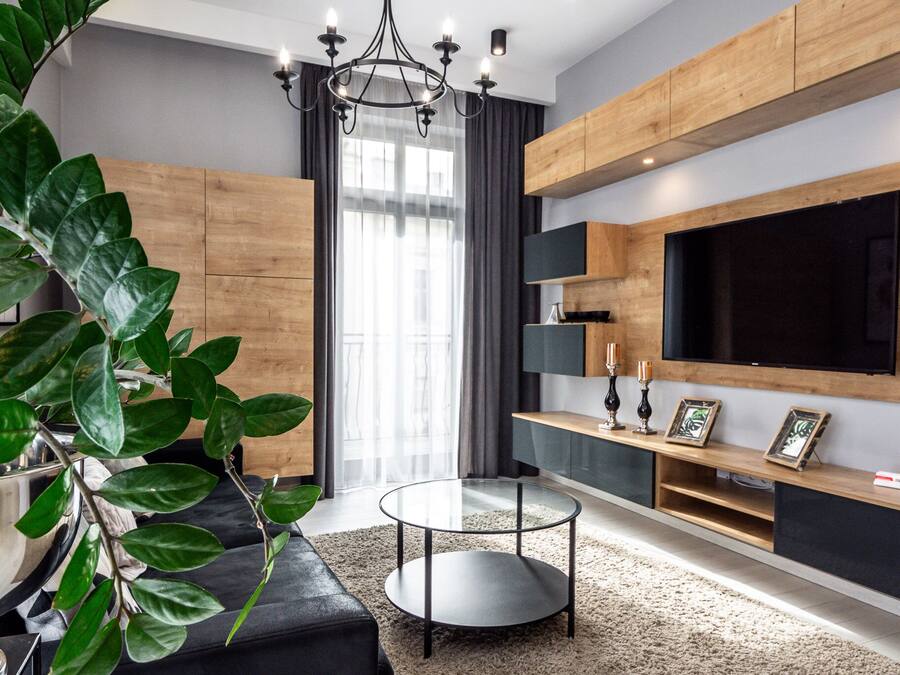 A modern living room with a black sofa, a round coffee table, a large TV, wooden cabinets, and a large green plant.