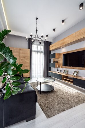 Un salon moderne avec un canapé noir, une table basse ronde, un grand téléviseur, des meubles en bois et une grande plante verte.
