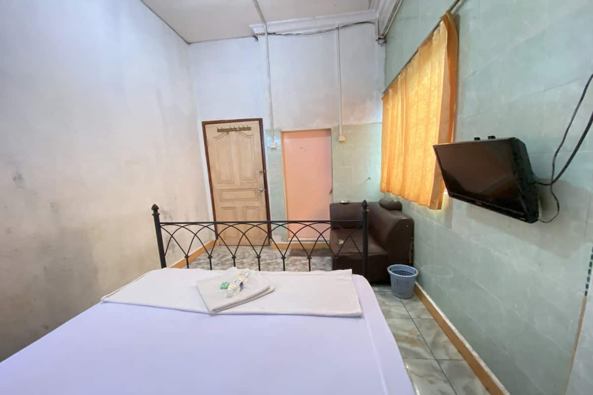 Una habitación con cama, televisor montado en la pared, una puerta y una ventana con cortinas.