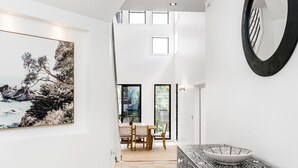 A modern interior with a dining area, a large abstract painting, and a view of the outdoors. - Byron Bay Accom - Sunset on Massinger - 60 Massinger Street - Pets on Request (Byron Bay)