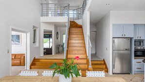 A modern kitchen with stainless steel appliances, a wooden staircase, and a dining area with a plant centerpiece. - Byron Bay Accom - Sunset on Massinger - 60 Massinger Street - Pets on Request (Byron Bay)