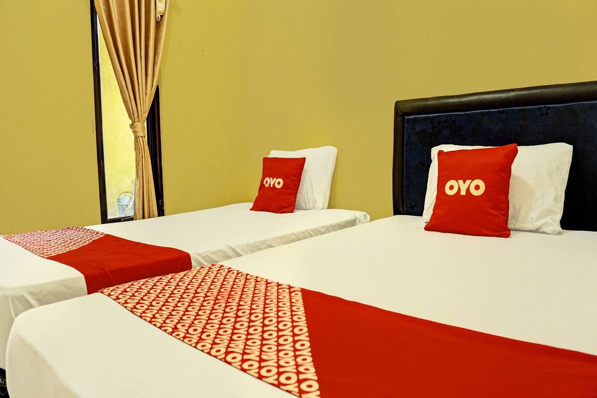 Een hotelkamer met twee bedden, elk met een rood-witte dekbedovertrek en kussens met de tekst 'OYO'.