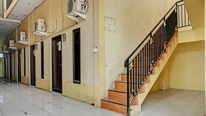 Un pasillo con una escalera que conduce a un piso superior, unidades de aire acondicionado instaladas en la pared y suelo de baldosas.