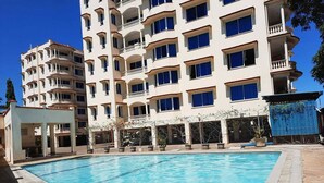 A hotel with a swimming pool, multiple balconies, and a clear blue sky. - Lux Suites Liz Royal Apartments Nyali (Mombasa)