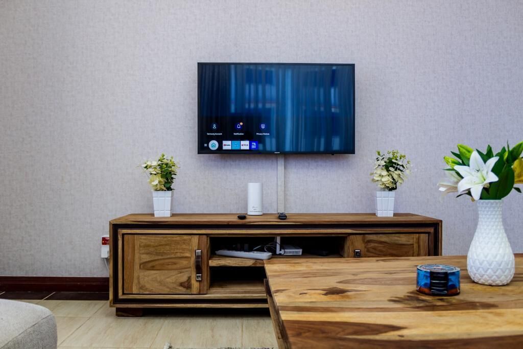 Ett modernt vardagsrum med en platt-TV som är monterad på väggen, en träinredd TV-möbel med ett skåp och två krukväxter.
