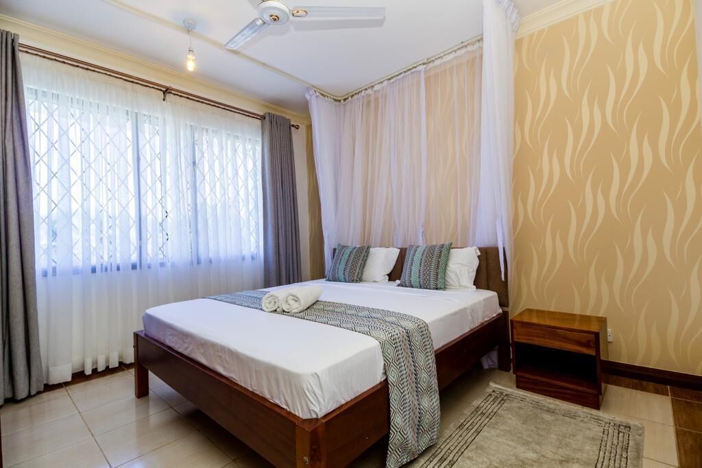 A bedroom with a large bed, a bedside table, a ceiling fan, and a window with curtains.