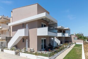 Un edificio residencial moderno de dos plantas con techo plano, ventanas amplias y un balcón con barandilla de metal.