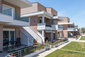 Un moderno edificio residencial de varios pisos con balcones, una zona de estar al aire libre techada y un césped bien cuidado.