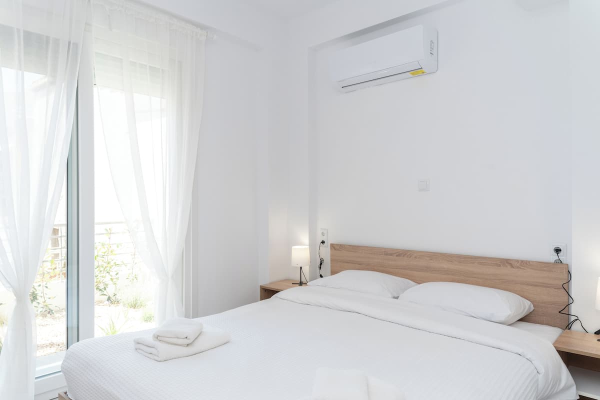 Una cama bien hecha con sábanas blancas, cabecera de madera y mesita de noche con lámpara.