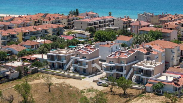 Una zona residencial costera con edificios de tejados de terracota, una playa de arena y una vista despejada del mar.