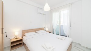 Una habitación de hotel moderna con una cama grande, mesitas de noche con lámparas, un equipo de aire acondicionado y vistas al exterior a través de cortinas translúcidas.
