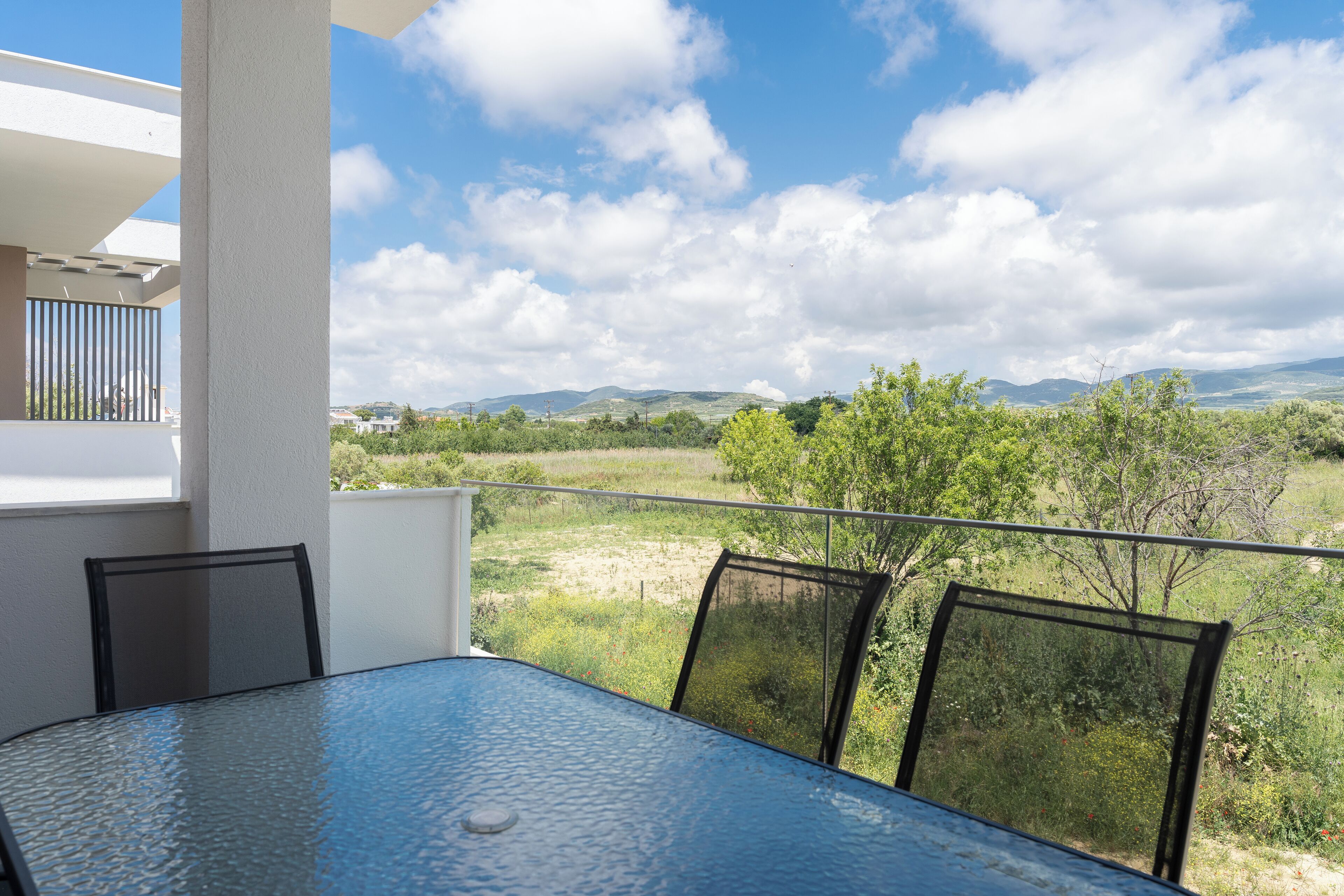 A balcony with a table and chairs, overlooking a landscape with trees and distant hills.