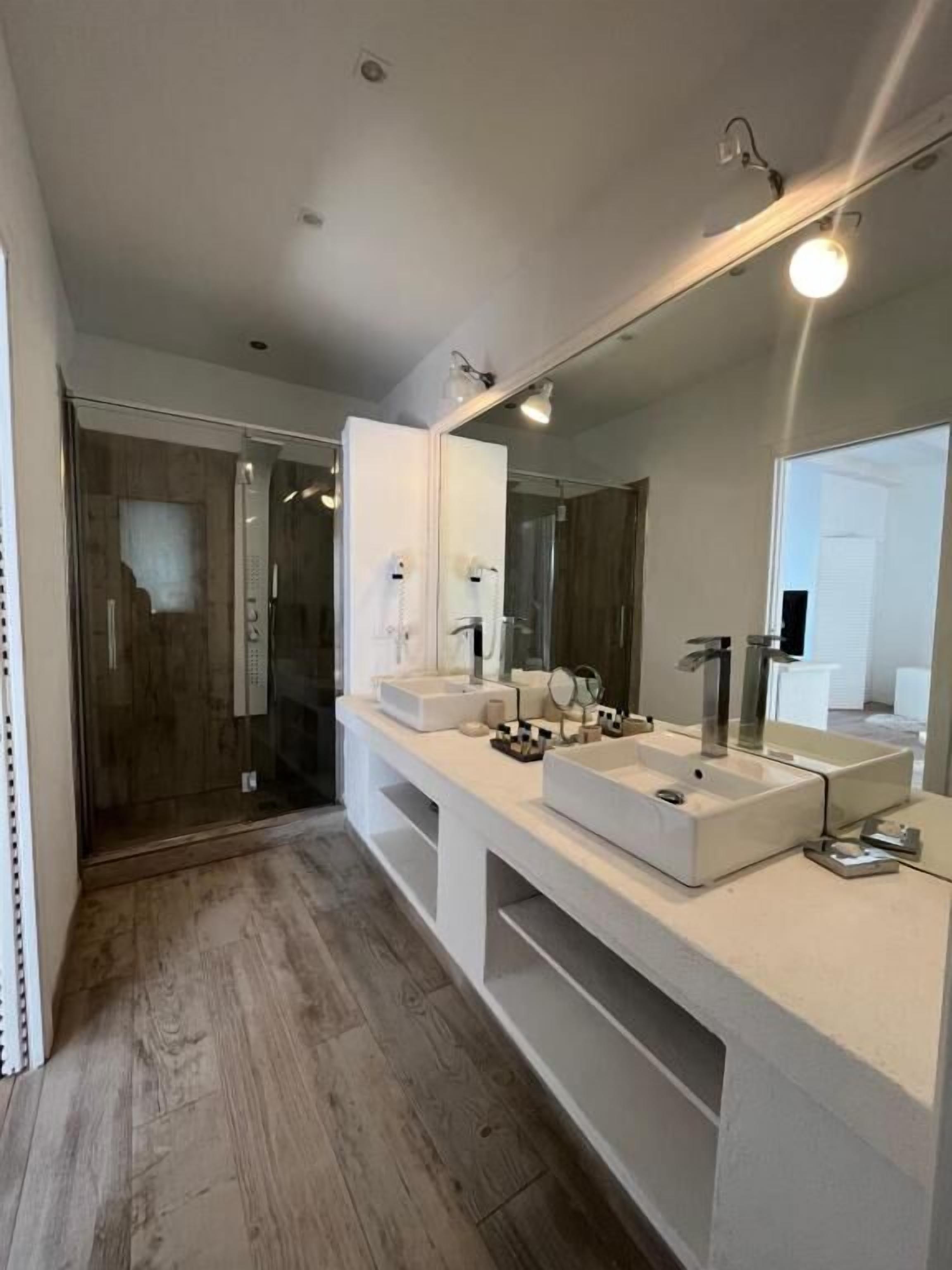 A modern bathroom with a large mirror, two sinks, and a shower area.