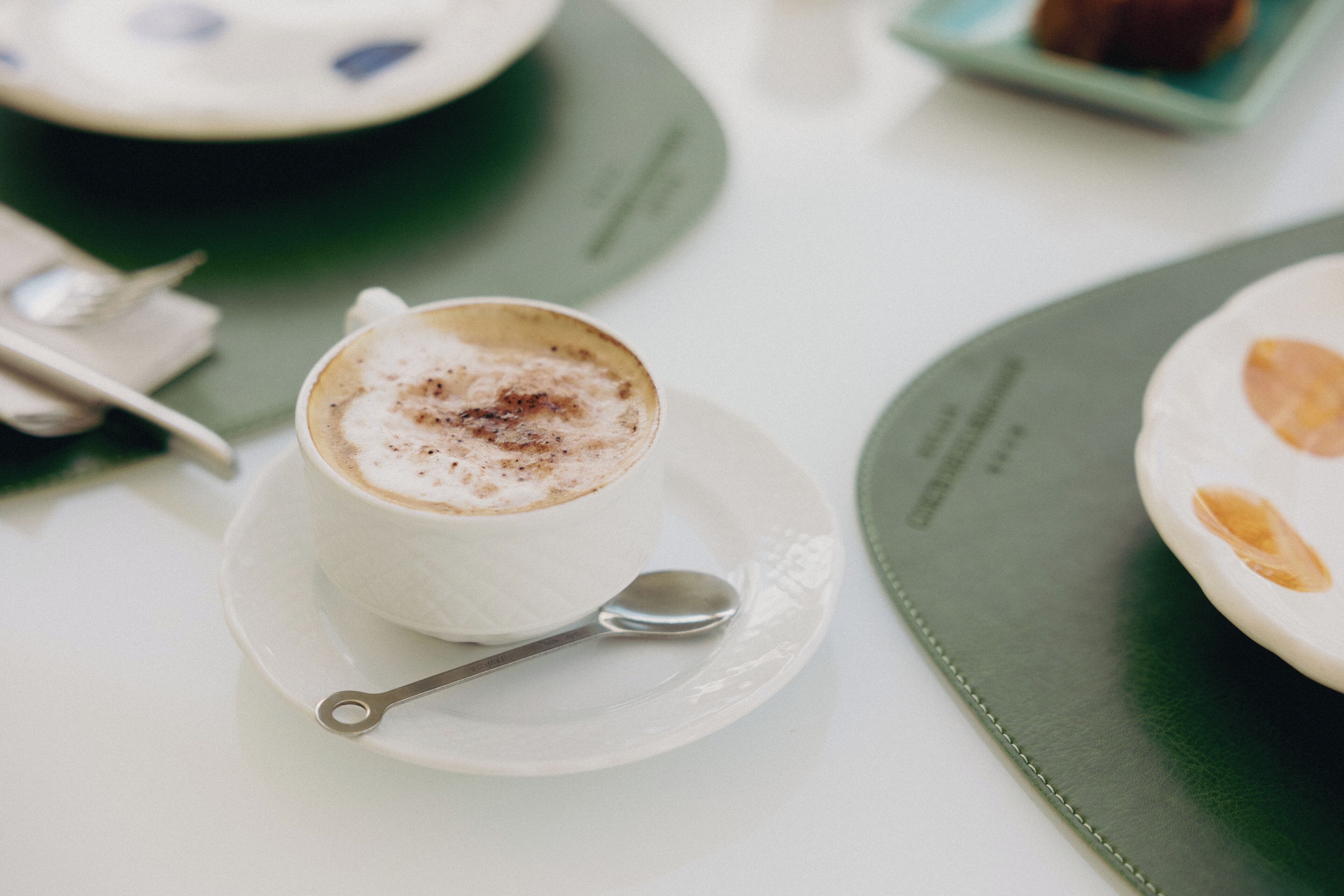 Une tasse de café avec une cuillère, posée sur une soucoupe, le tout placé sur une table recouverte d’un set de table vert.
