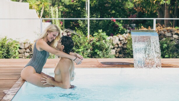 A couple by a pool with a waterfall feature, surrounded by greenery and a stone wall. - Relais Corte degli Aragonesi (Ischia)