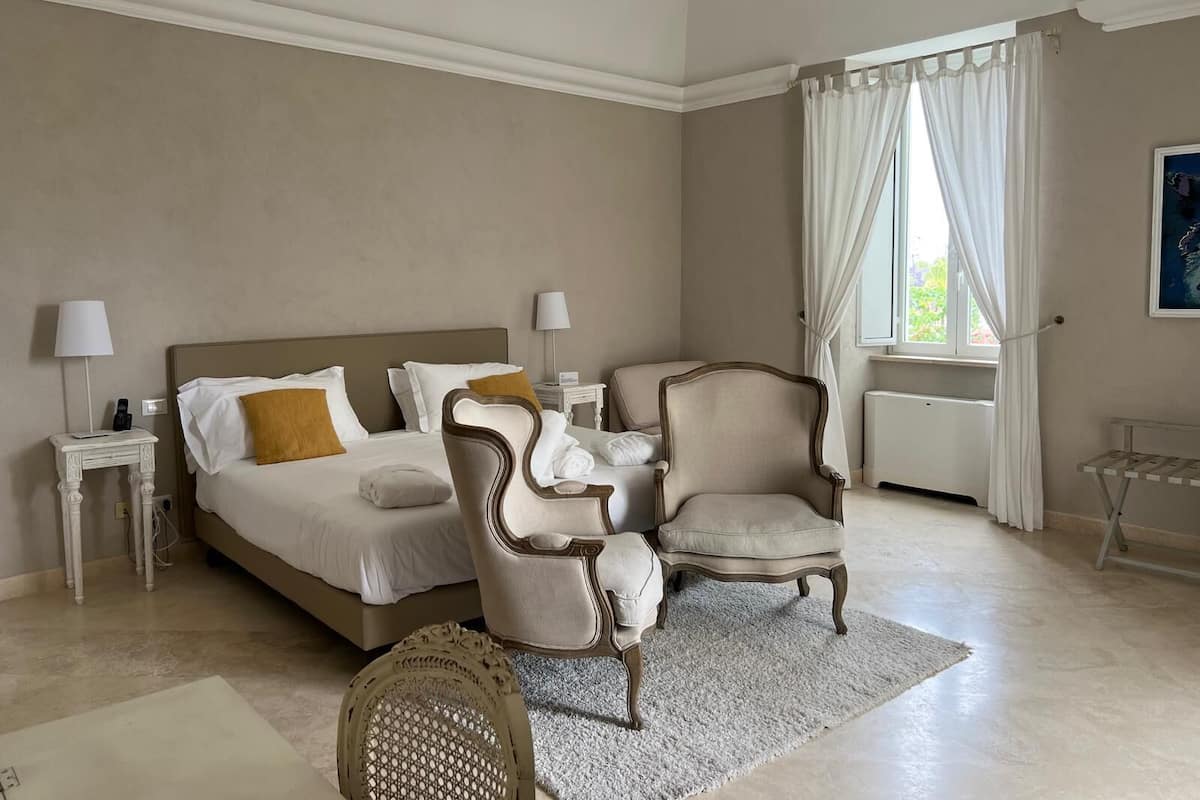Ein Schlafzimmer mit einem Bett, zwei Stühlen, einem kleinen Tisch und einem Fenster mit Vorhängen.