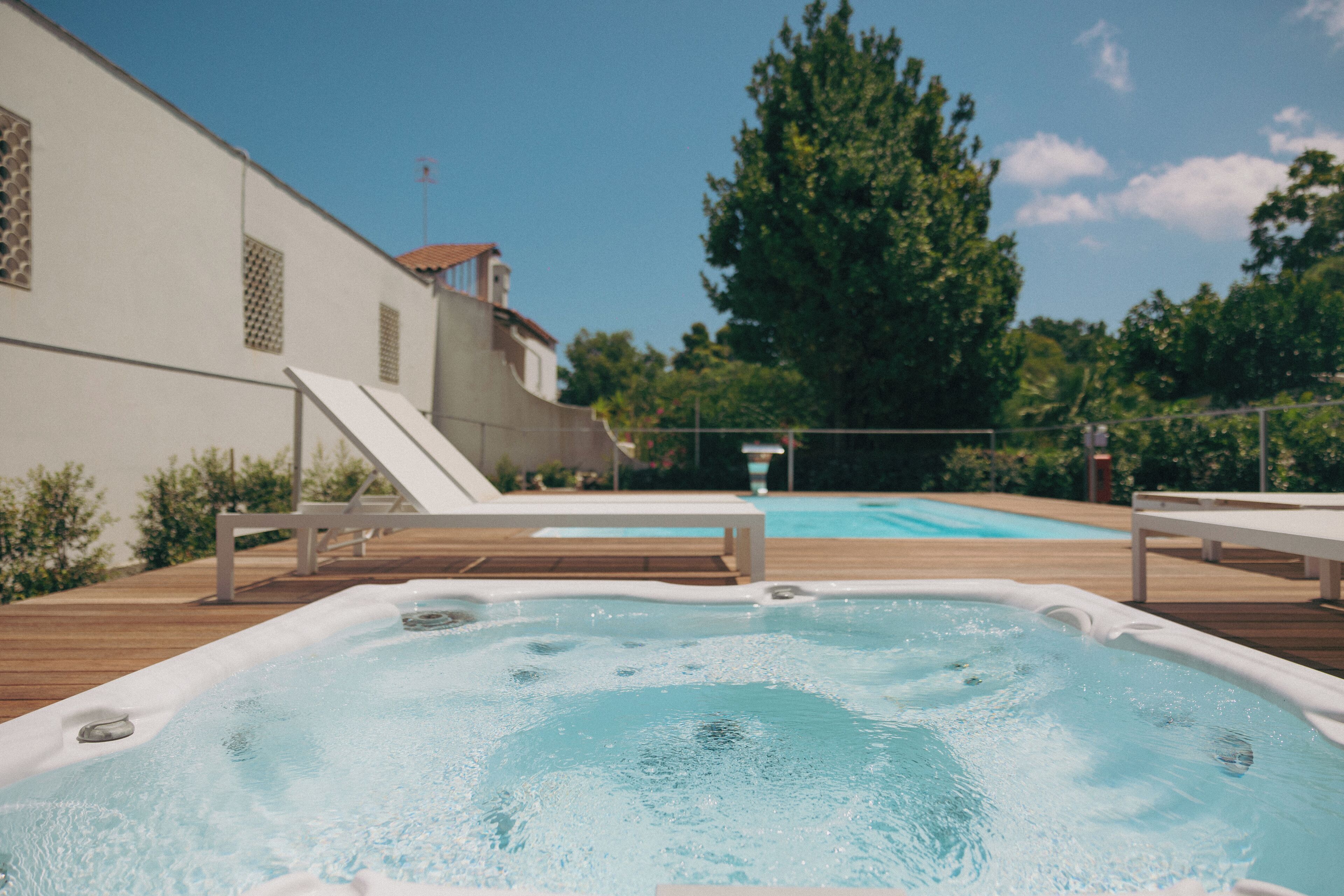 A hot tub with a wooden deck and a pool in the background.