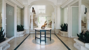 A grand hallway with a marble floor, white columns, and a central table with a sculpture. - Relais Corte degli Aragonesi (Ischia)