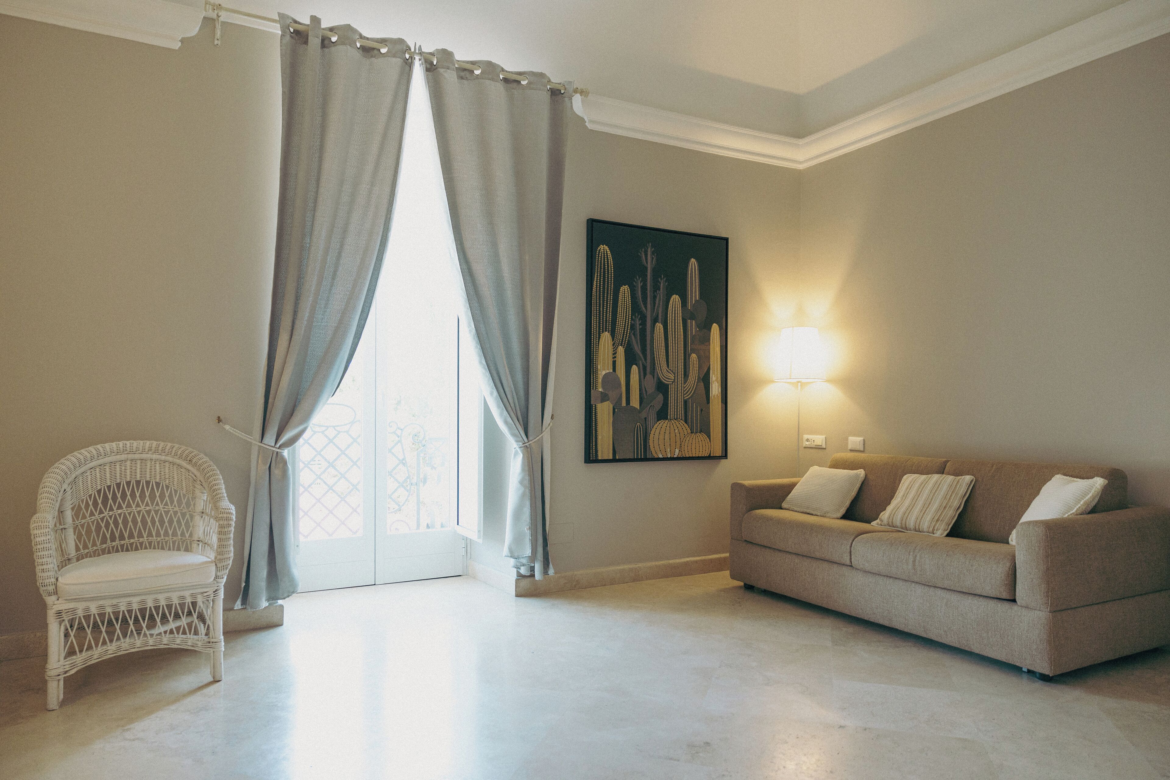 A living room with a white wicker chair, a beige sofa, a large abstract painting, and a floor lamp.