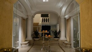 A grand hallway with a high ceiling, white columns, and a staircase leading to an upper level. There are potted plants and a decorative table with candles. - Relais Corte degli Aragonesi (Ischia)