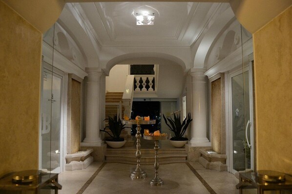 A grand hallway with a high ceiling, white columns, and a staircase leading to an upper level. There are potted plants and a decorative table with candles. - Relais Corte degli Aragonesi (Ischia)
