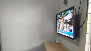 Ein an der Wand befestigter Fernseher, darunter ein Holzregal und eine Fernbedienung auf dem Regal.