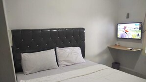 Ein Hotelzimmer mit einem Bett, einem an der Wand montierten Fernseher und einer kleinen Ablage mit einer Fernbedienung.