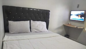 Ein ordentlich bezogenes Bett mit weißer Bettwäsche und einem gesteppten Kopfteil.