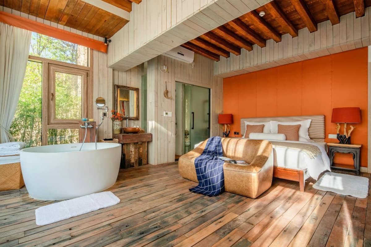 Une chambre avec une grande baignoire, un canapé, un lit et une table de chevet avec des lampes.