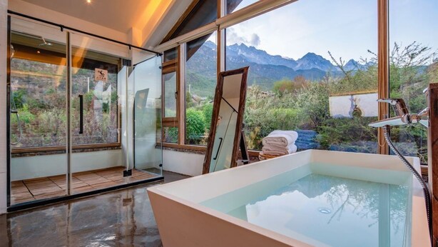 Een moderne spa ruimte met een groot bad, glazen deuren en uitzicht op de bergen.
