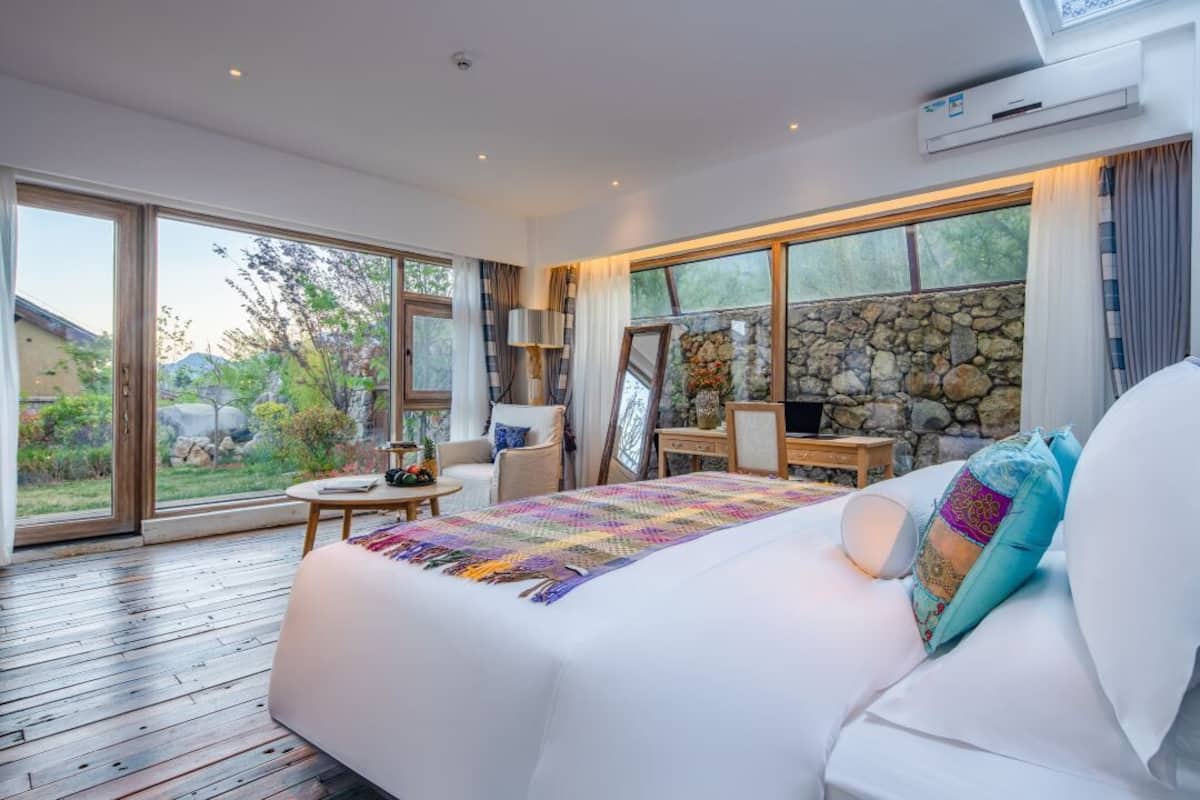 Une chambre spacieuse avec un grand lit, un mur en pierre et une vue sur l’extérieur.