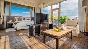 Een ruime kamer met een bed, een televisie, een houten salontafel met fruit en een balkon met uitzicht.
