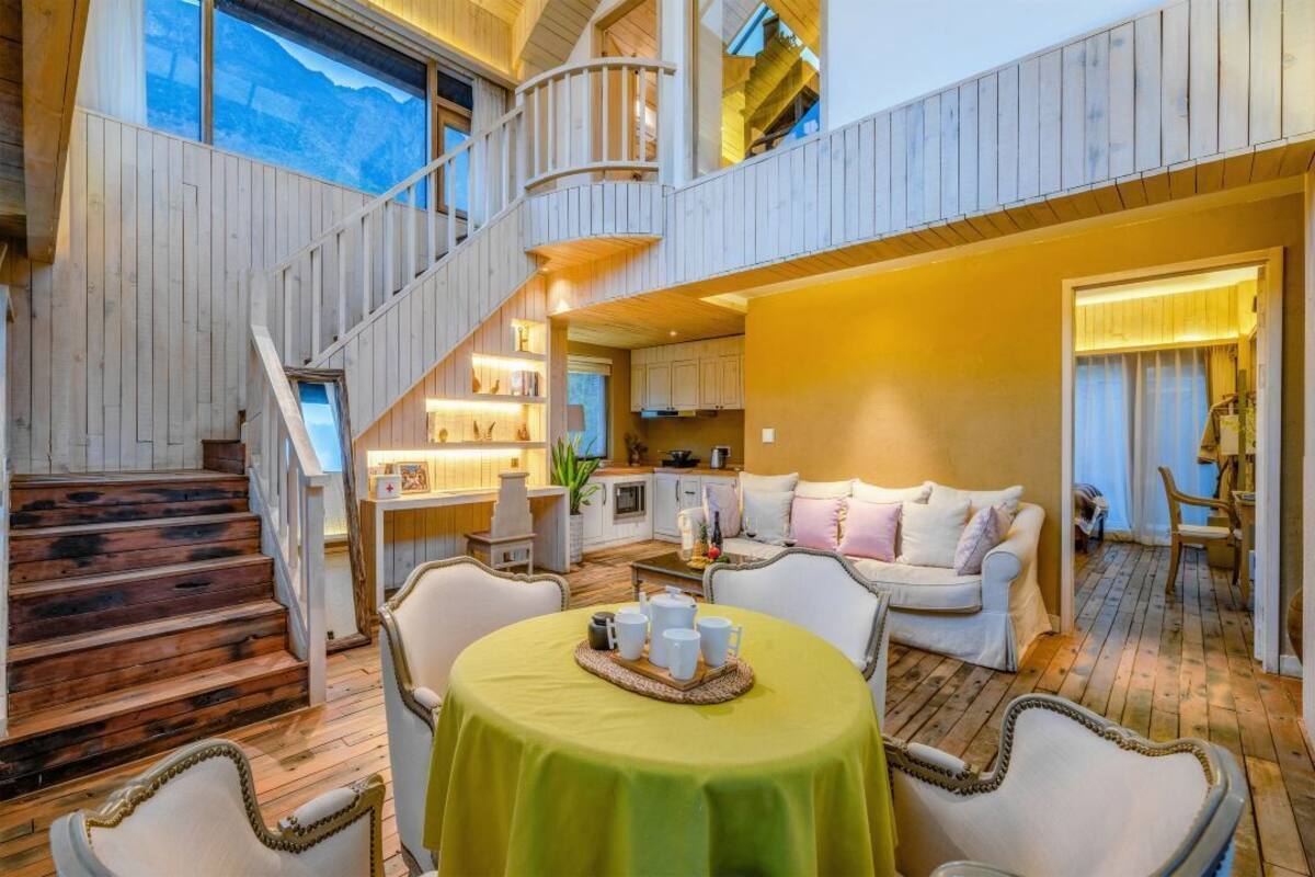 Un intérieur en bois à plusieurs niveaux, avec un escalier, un coin repas avec une table dressée pour deux personnes et un espace salon confortable avec un canapé et des fauteuils.