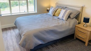 Une chambre à coucher avec un lit, deux tables de chevet, une fenêtre et une vue sur la verdure.