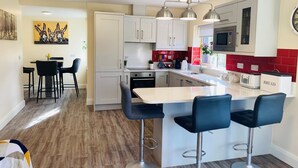 Une cuisine moderne avec des meubles blancs, un îlot central doté de tabourets, un pare-feu rouge et un coin repas avec une table et des chaises.