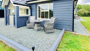 Une maison dotée d’un patio comprenant deux fauteuils en osier et une table, le tout entouré de gravier et d’un petit jardin.