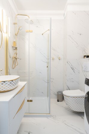 Bathroom features a glass-enclosed shower with handheld and rain showerheads, a white vanity, and a round sink.
