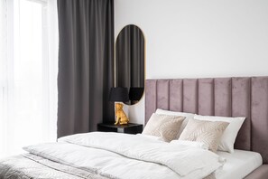 Relax in a serene bedroom with a plush bed, soft headboard, and elegant mirror.