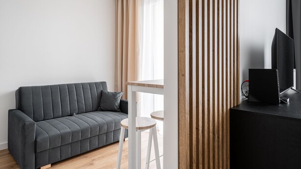 Un salon moderne avec un canapé gris, une petite table ronde et un téléviseur posé sur un meuble noir.