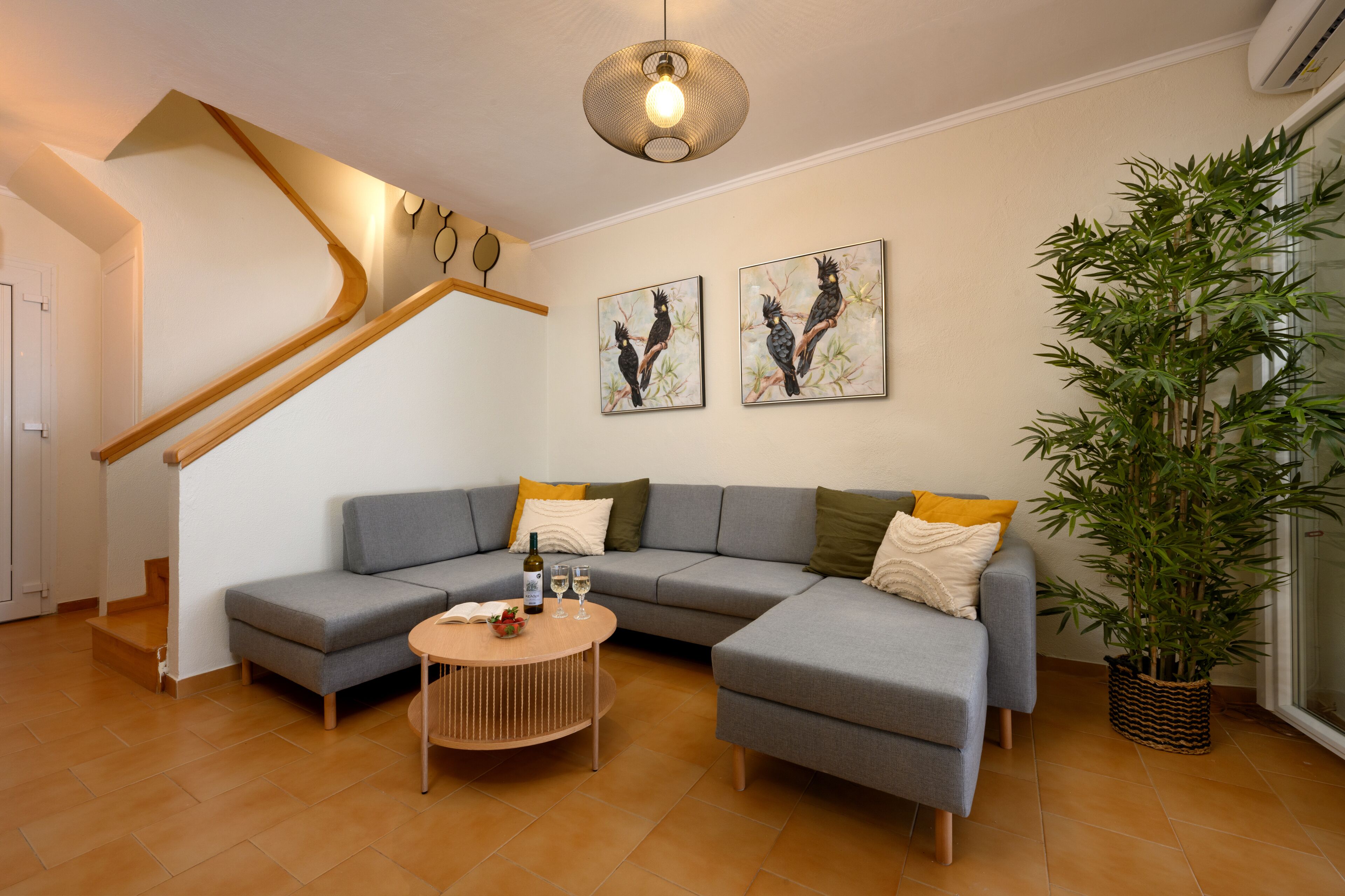 Ein modernes Wohnzimmer mit einem grauen Ecksofa, einem runden Couchtisch und einer großen Kühlpflanze.