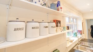 A kitchen with white shelves holding kitchenware, including jars labeled "ARROZ," "MASSA," "FARINHA," and "FEIJAO."
