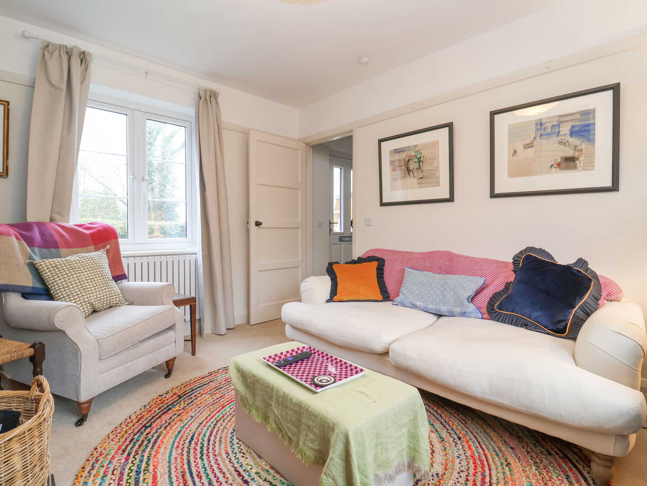 Ein Wohnzimmer mit einem weißen Sofa, einem gemusterten Sessel, einem farbenfrohen Teppich und zwei gerahmten Bildern an der Wand.