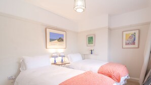 A hotel room with two beds, a nightstand with lamps, and framed artwork on the walls.