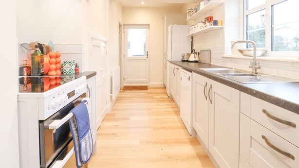 A modern kitchen with white cabinets, a wooden floor, a built-in oven, and a window providing natural light.