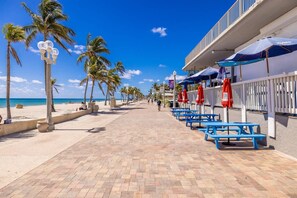 A beachfront walkway with palm trees, benches, and umbrellas.