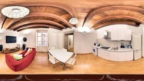 Ein geräumiger Wohnbereich mit einem roten Sofa, einem Esstisch und einer Küche mit weißen Schränken und einer Spüle.