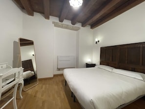 Une chambre avec un plafond en bois, un lit avec une literie blanche, une table de chevet avec une lampe, une commode et un miroir.