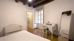 Ein Schlafzimmer mit einem Bett, einer weißen Kommode, einem Sessel, einem Spiegel und einer Klimaanlage.