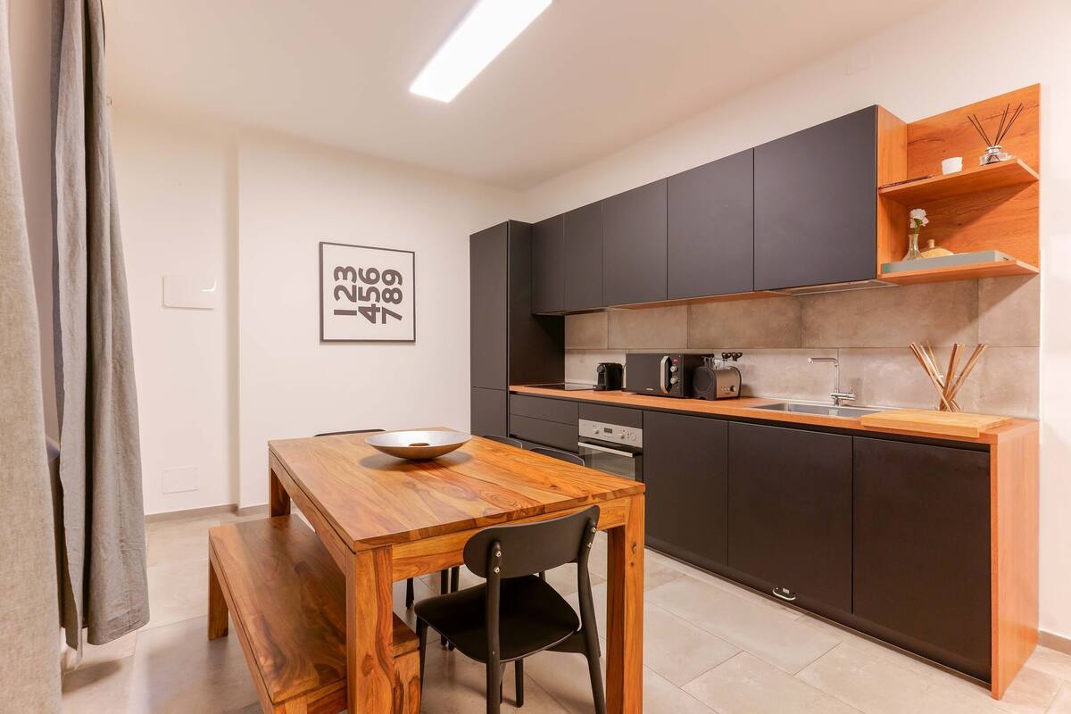Una cocina moderna con armarios oscuros, una mesa de comedor de madera y un banco.