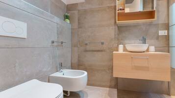 Une salle de bain moderne équipée d’un bidet, de toilettes, d’un lavabo et d’un miroir.